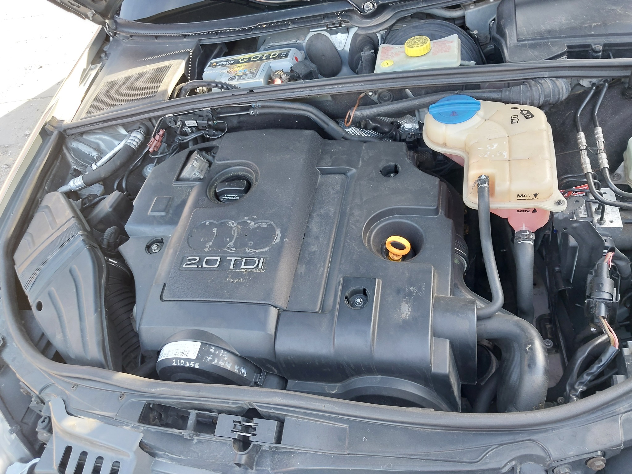 Otwarta maska samochodu Audi z widocznym silnikiem 2.0 TDI, zbiornikiem płynu chłodniczego z niebieską zakrętką i akumulatorem Jenox Gold.