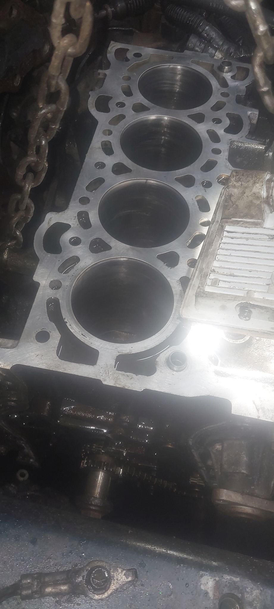 Odsłonięty blok silnika z widocznymi cylindrami, łańcuch rozrządu i elementy osprzętu, w trakcie naprawy lub remontu w warsztacie.