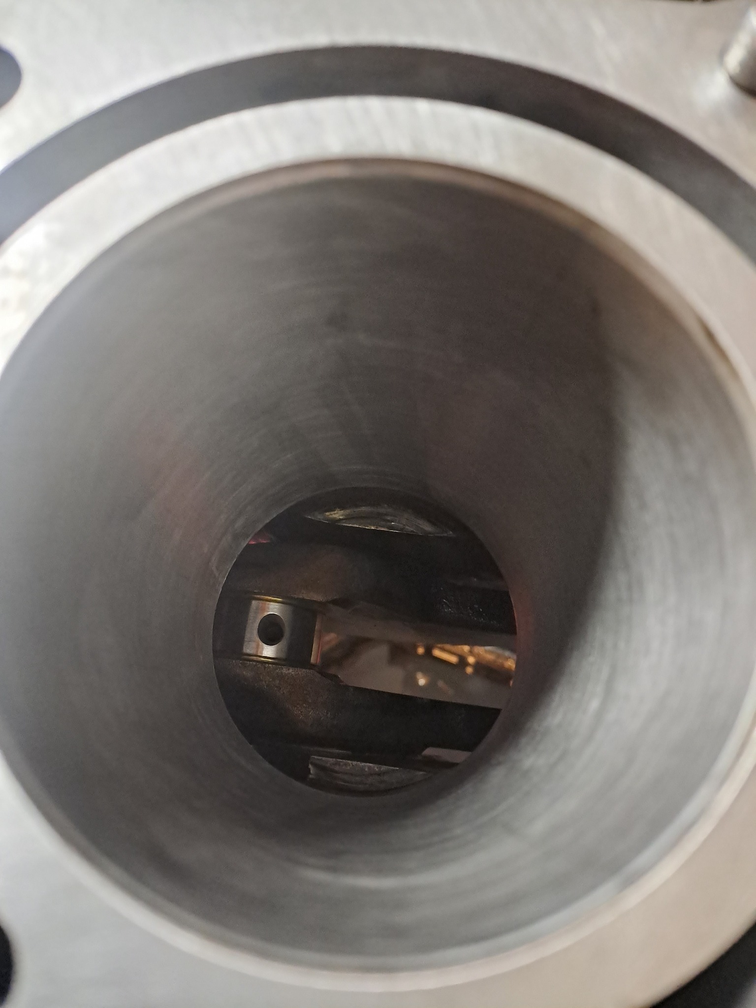 Wnętrze cylindra silnika spalinowego, widoczny tłok i korbowód w słabym oświetleniu warsztatowym.