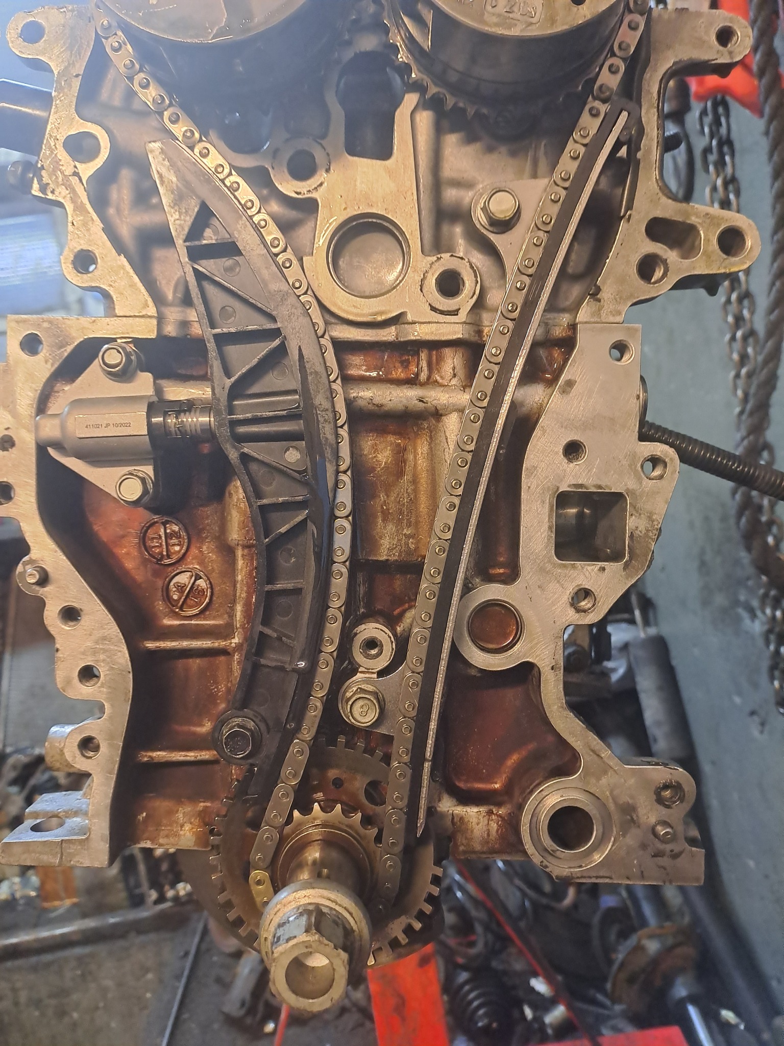 Widok z bliska na otwarty silnik samochodowy z widocznym łańcuchem rozrządu, z wyraźnymi śladami oleju i zużycia.