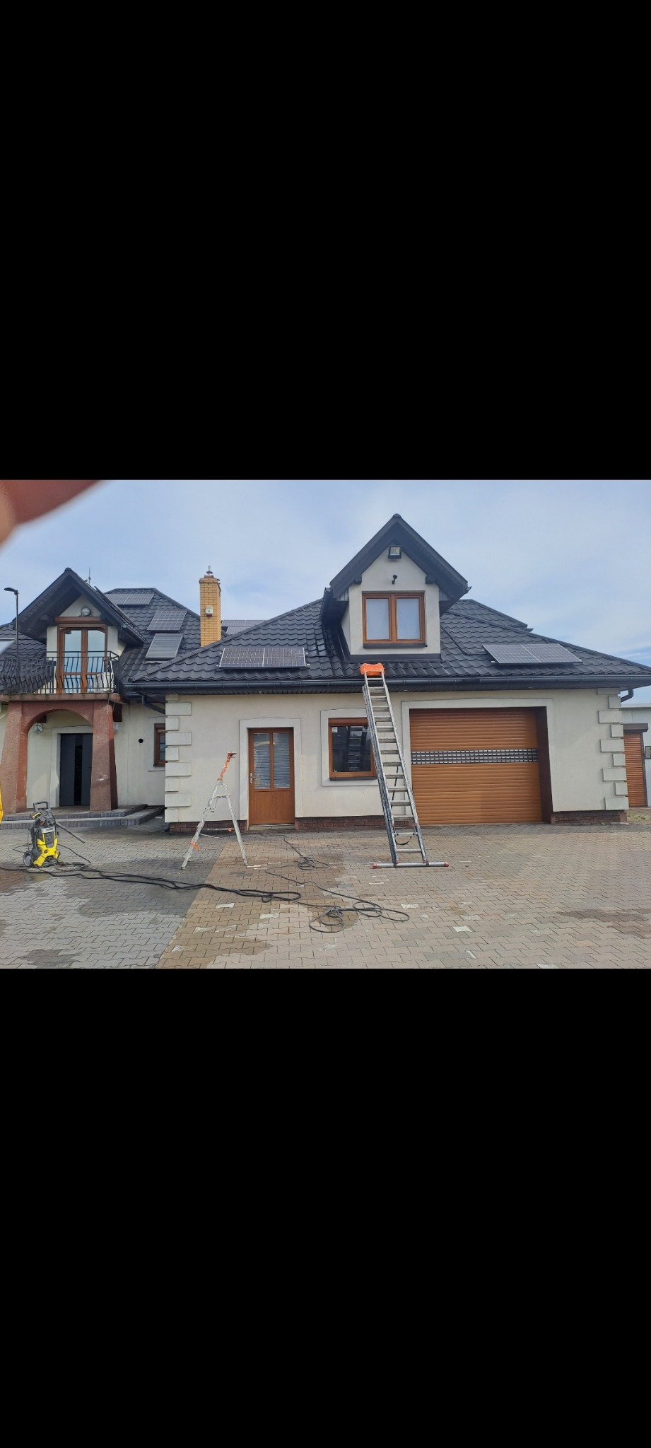 Elewacja domu jednorodzinnego z panelami słonecznymi, przygotowana do malowania w Błoniu. Widoczny sprzęt do czyszczenia i drabiny.