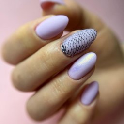 YokoNail - Salon Kosmetyczny - Manicure & Pedicure - Dłoń z pastelowymi, liliowymi paznokciami; jeden z nich zdobiony czarną siateczką i rzędem małych, srebrnych dżetów przy skórkach.