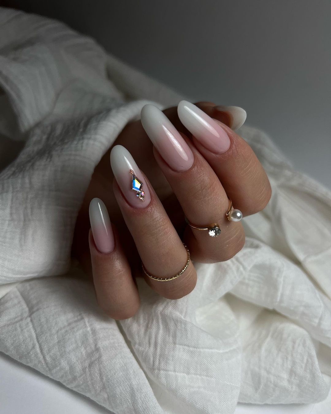 Delikatne, ombre paznokcie w odcieniach bieli i różu, zdobione drobnymi kryształkami, prezentowane na dłoni z pierścionkami w Tarnowie Podgórnym.