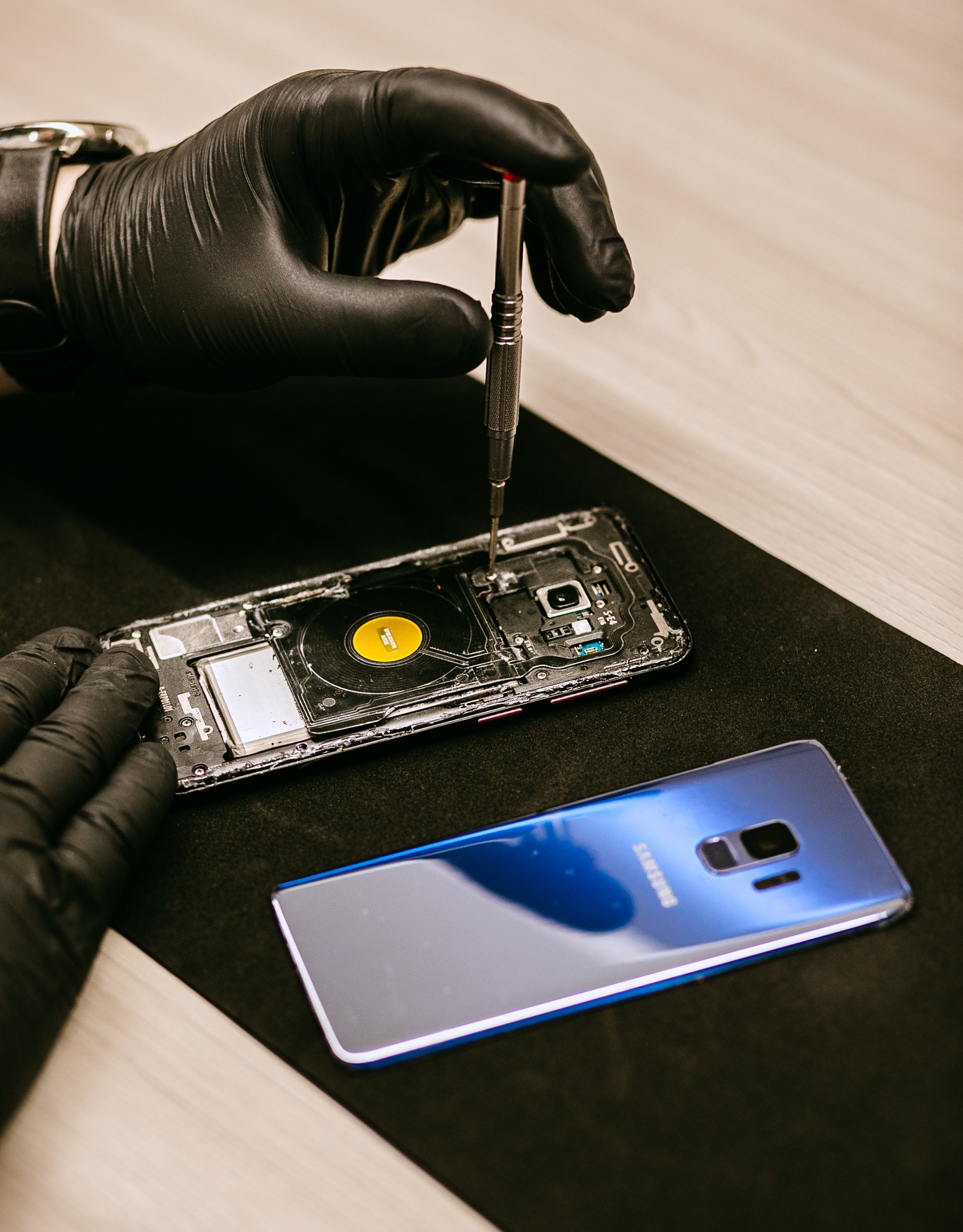 Otwarty smartfon Samsung Galaxy S9 z widocznymi podzespołami naprawiany precyzyjnym śrubokrętem przez technika w czarnych rękawiczkach; obok leży niebieska obudowa.
