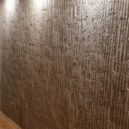 Dekoracyjna ściana z pionowych, wąskich elementów imitujących kamień, oświetlona punktowymi lampami sufitowymi, z widoczną częścią drewnianej podłogi.