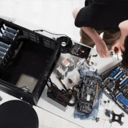Osoba montuje chłodzenie procesora na płycie głównej komputera stacjonarnego, obok rozłożone podzespoły i obudowa na białym biurku.