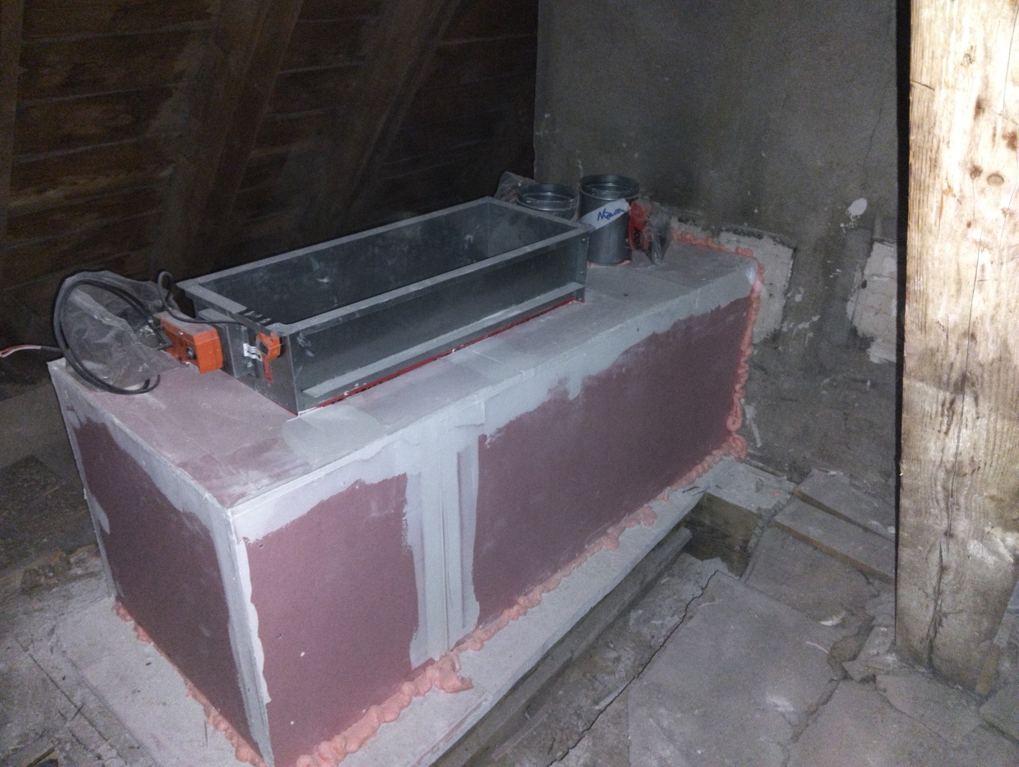 Wnętrze poddasza z widoczną skrzynką rozprężną wentylacji, zabezpieczoną pianką montażową i obudowaną płytami gipsowo-kartonowymi, obok stoją puszki i narzędzia.