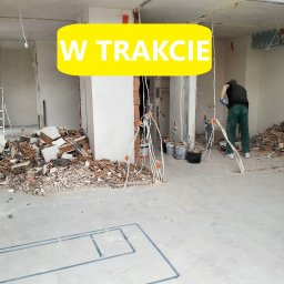 MK-BUD Mateusz Kocięda - Demontaż ściany w trakcie: widoczne gruzowisko, odsłonięte przewody elektryczne, zarys planu pomieszczenia na podłodze oraz pracownik w tle.