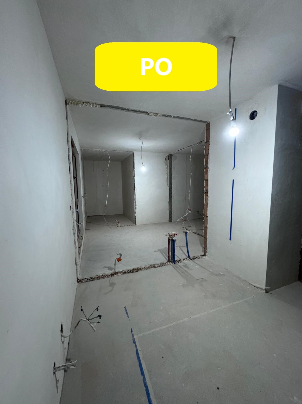 Wnętrze po usunięciu ścian działowych, widoczne odsłonięte przewody elektryczne i rury instalacyjne, ślady po wyburzeniach na podłodze i ścianach, surowy beton na podłodze, w tle kolejne...