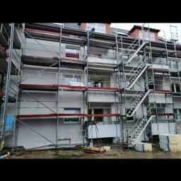 Zakład ogolnobudowlany Rzepka Tomasz Stanisław - Wielopiętrowy budynek mieszkalny w trakcie ocieplania, z rusztowaniami i widocznymi płytami styropianowymi na palecie.