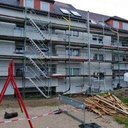 Zakład ogolnobudowlany Rzepka Tomasz Stanisław - Wielopiętrowy budynek mieszkalny w trakcie prac elewacyjnych, otoczony rusztowaniami i zabezpieczeniami, z widocznym stosem drewna i elementami konstrukcyjnymi na pierwszym planie.