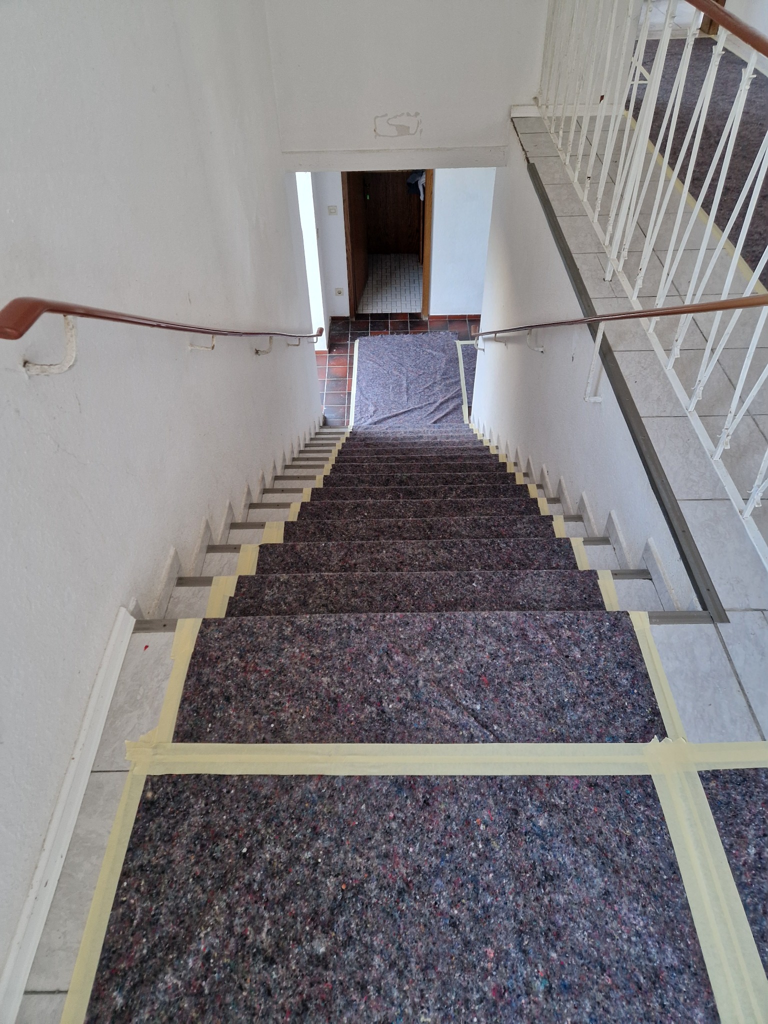 Klatka schodowa zabezpieczona folią malarską i taśmą przed rozpoczęciem prac, widok z góry.
