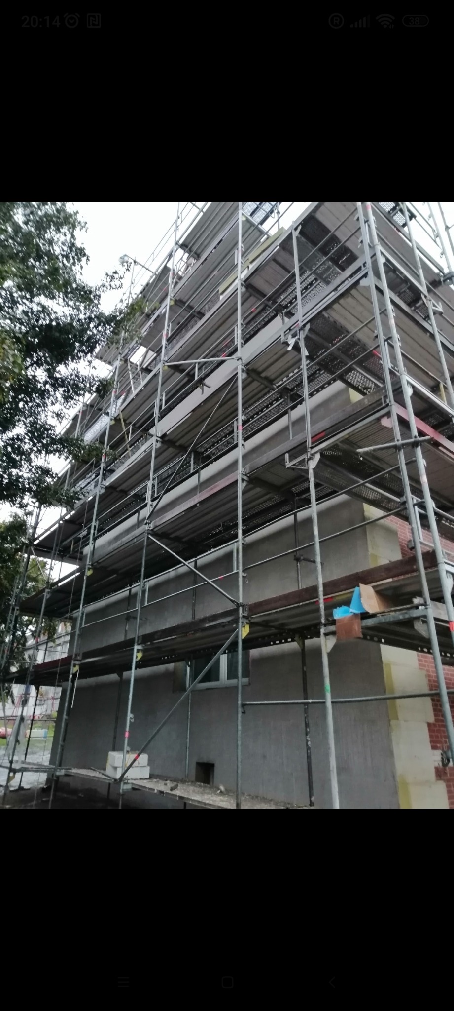 Budynek w trakcie prac elewacyjnych, z widocznym rusztowaniem i fragmentami ocieplenia oraz nowej elewacji.