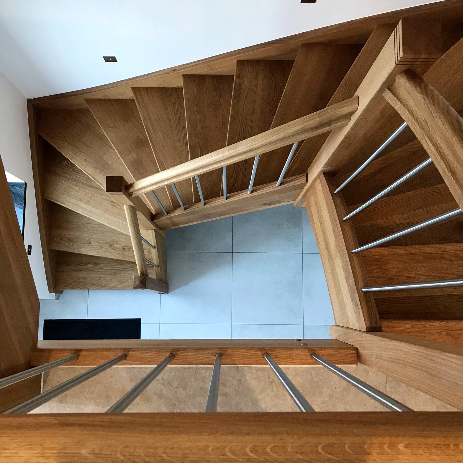 Drewniane schody z metalowymi barierkami widziane z góry w domu w Strzegomiu, z widocznymi płytkami podłogowymi na obu poziomach.