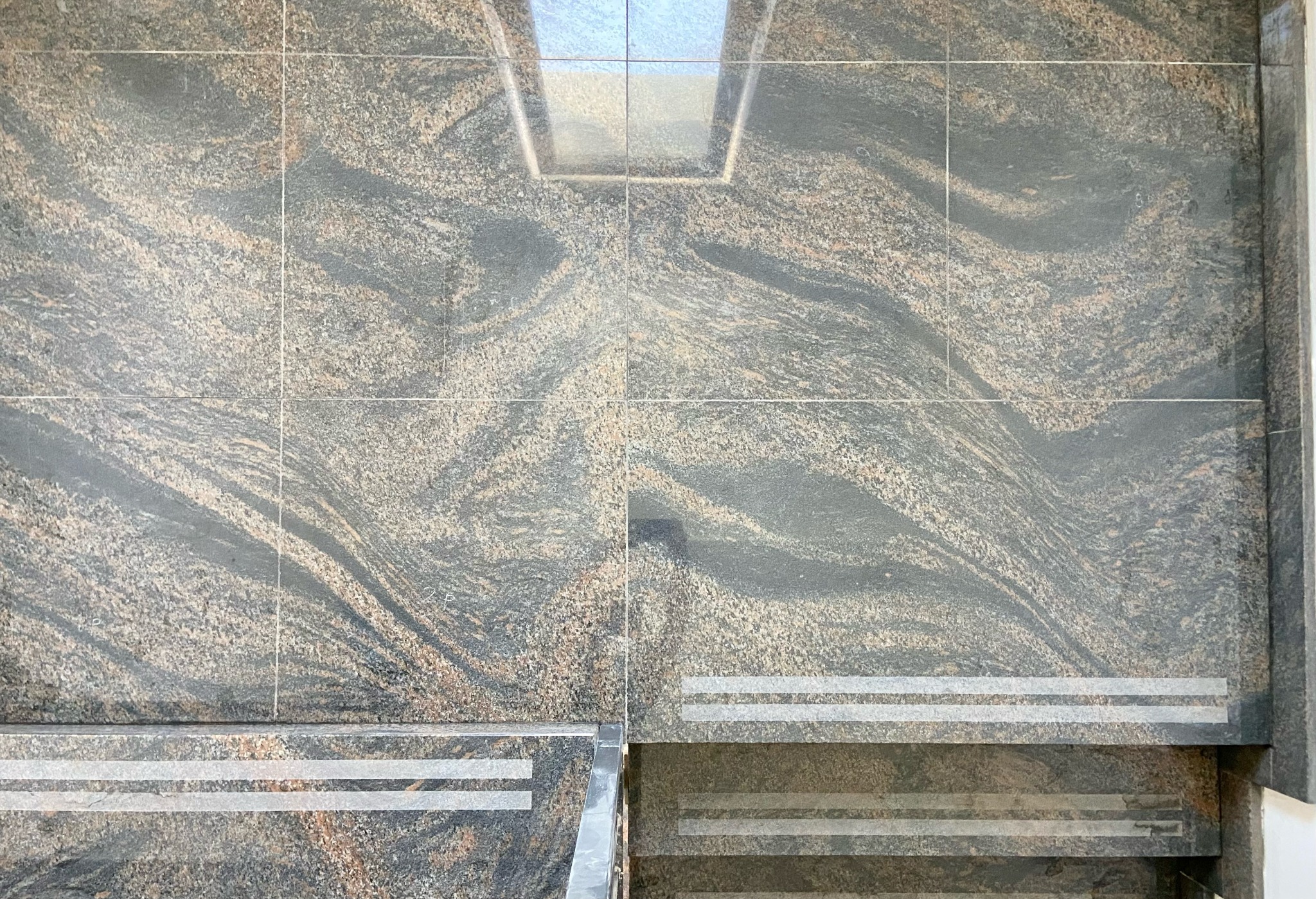 Wykończone schody i podłoga z płytek imitujących kamień o wzorze przypominającym fale, z antypoślizgowymi paskami na krawędziach stopni i odbiciem światła w górnej części.