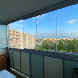 OMEGA Krzysztof Byckiewicz - Zabudowany balkon z przesuwnymi szklanymi panelami, widok na osiedle mieszkaniowe w pogodny dzień.