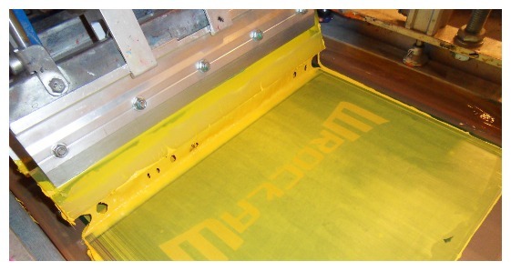 Sito z nałożoną żółtą farbą i raklem gotowe do nadruku wzoru na odzieży.