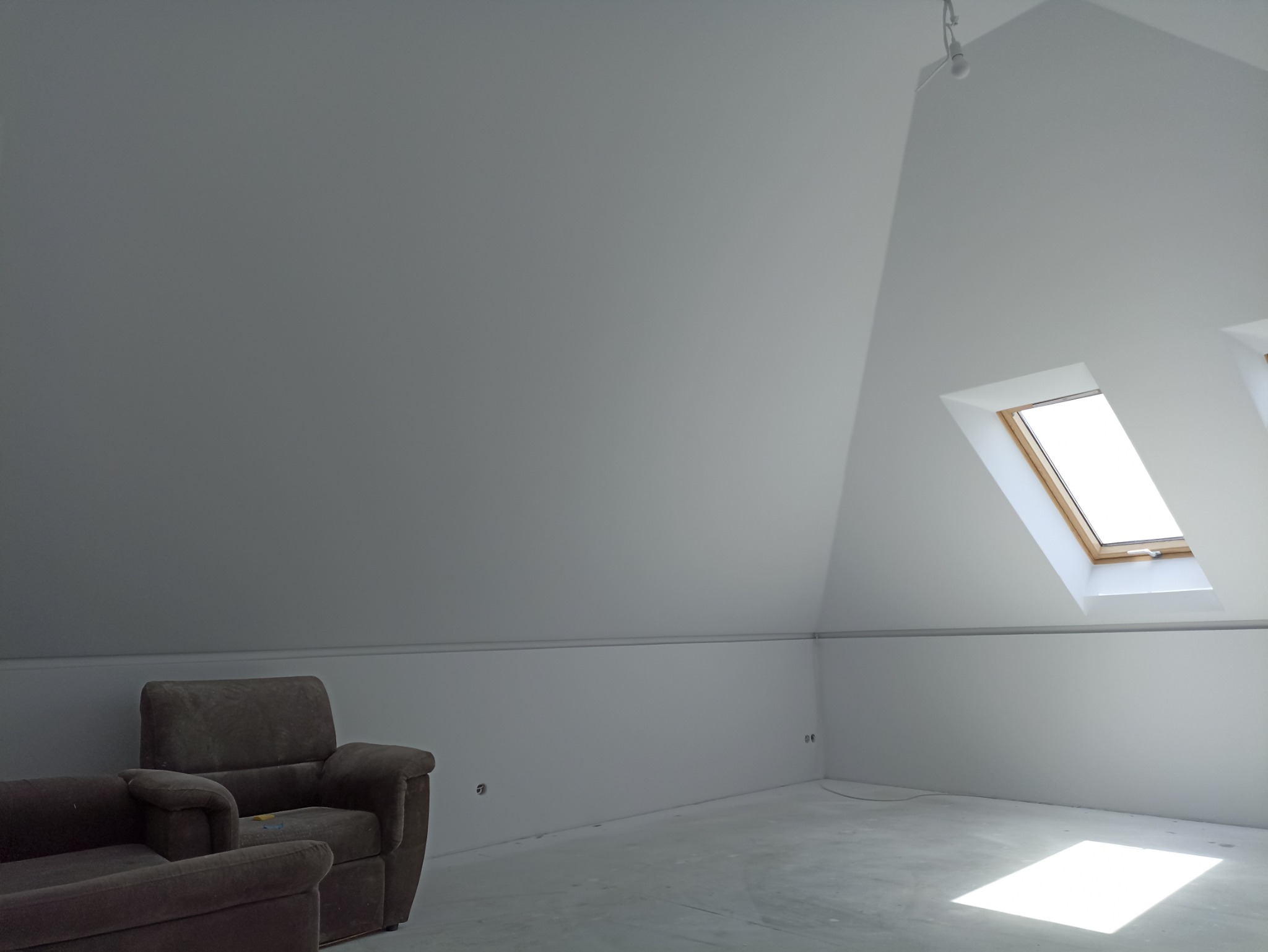 Poddasze po remoncie w Gorzowie Wielkopolskim z oknami dachowymi, pomalowane na biało, z widocznymi fotelami i surową podłogą przygotowaną do dalszych prac wykończeniowych.