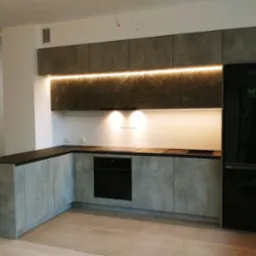 Nowoczesna kuchnia na wymiar z szarymi frontami imitującymi beton, czarnym blatem, oświetleniem LED podszafkowym i czarną lod&oacute;wką Samsung.