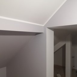 Tynki maszynowe - Szare ściany i biały sufit po remoncie poddasza. Widoczne narożniki i fragmenty instalacji w głębi. Minimalistyczne wykończenie.