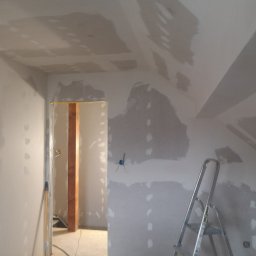 Tynki maszynowe - Poddasze w trakcie prac wykończeniowych: ściany i sufit pokryte gładzią szpachlową, widoczna drabina i otwór drzwiowy z drewnianą ościeżnicą.