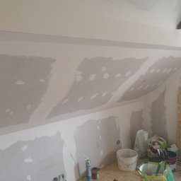 Tynki maszynowe - Poddasze w trakcie szpachlowania: widoczne płyty gipsowo-kartonowe na skosach, częściowo pokryte szpachlą. Na podłodze narzędzia i materiały budowlane.