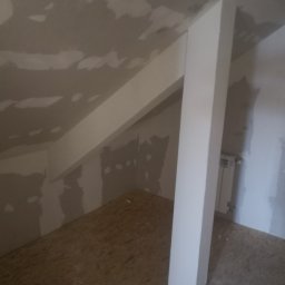 Tynki maszynowe - Poddasze w trakcie szpachlowania: ściany i skośny sufit z widocznymi łatami szpachli, drewniana podłoga, biały filar. W tle grzejnik.