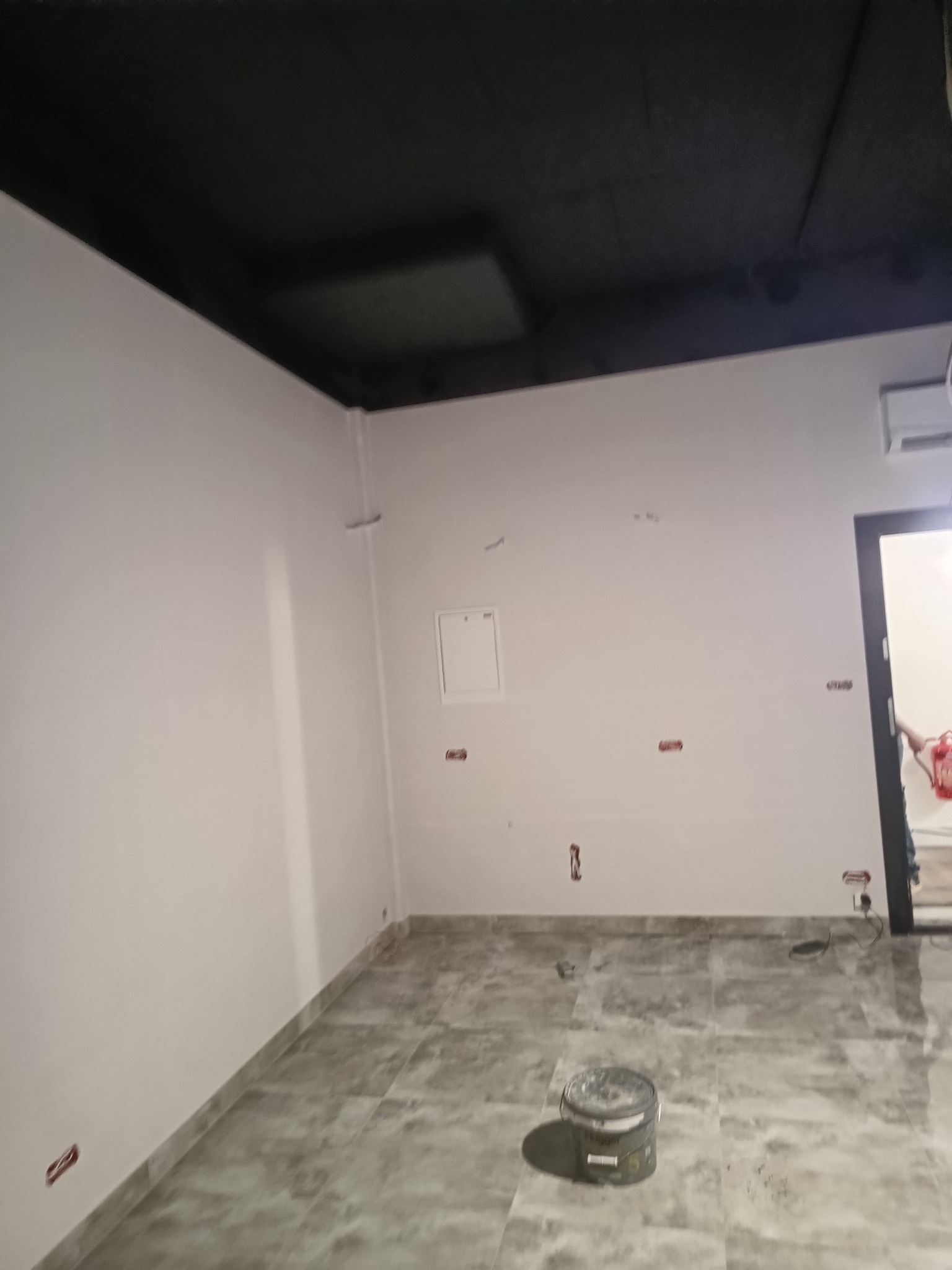 Wnętrze po malowaniu: białe ściany, czarny sufit, szara podłoga z płytek. Widoczny pojemnik z farbą na podłodze. Świeżo pomalowane pomieszczenie z przygotowanymi gniazdkami.