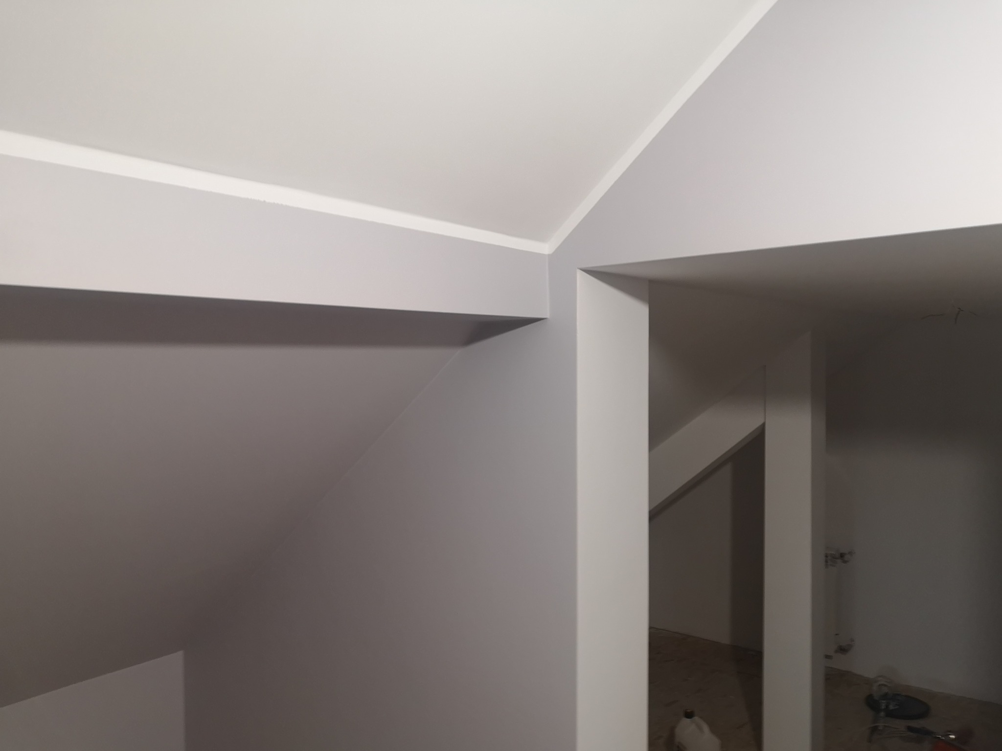 Szare ściany i biały sufit po remoncie poddasza. Widoczne narożniki i fragmenty instalacji w głębi. Minimalistyczne wykończenie.