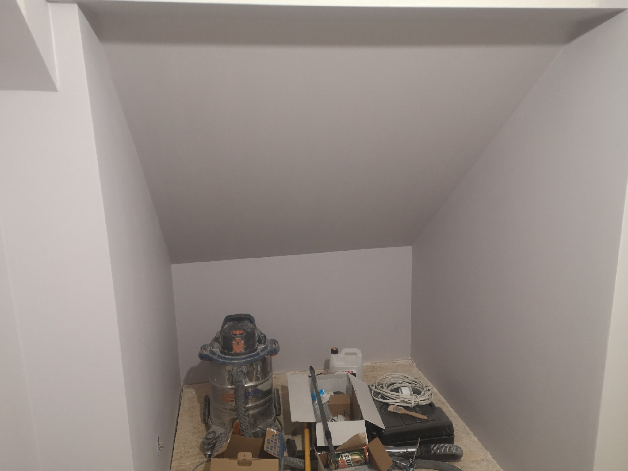Poddasze po malowaniu na szaro, widoczny odkurzacz przemysłowy i narzędzia malarskie. Świeżo pomalowane ściany w skośnym pomieszczeniu.