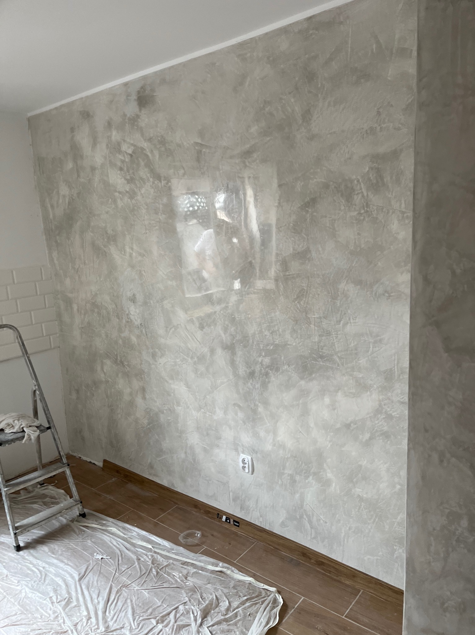 Ściana w szarościach z efektem dekoracyjnym, zabezpieczona podłoga, drabina w rogu. Widoczny kontakt elektryczny i listwa przypodłogowa. Wykończenie wnętrza w trakcie.