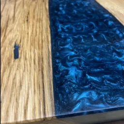Fragment blatu z drewna dębowego połączonego z żywicą epoksydową w odcieniach błękitu, widoczne unikalne słoje drewna i wzory żywicy.
