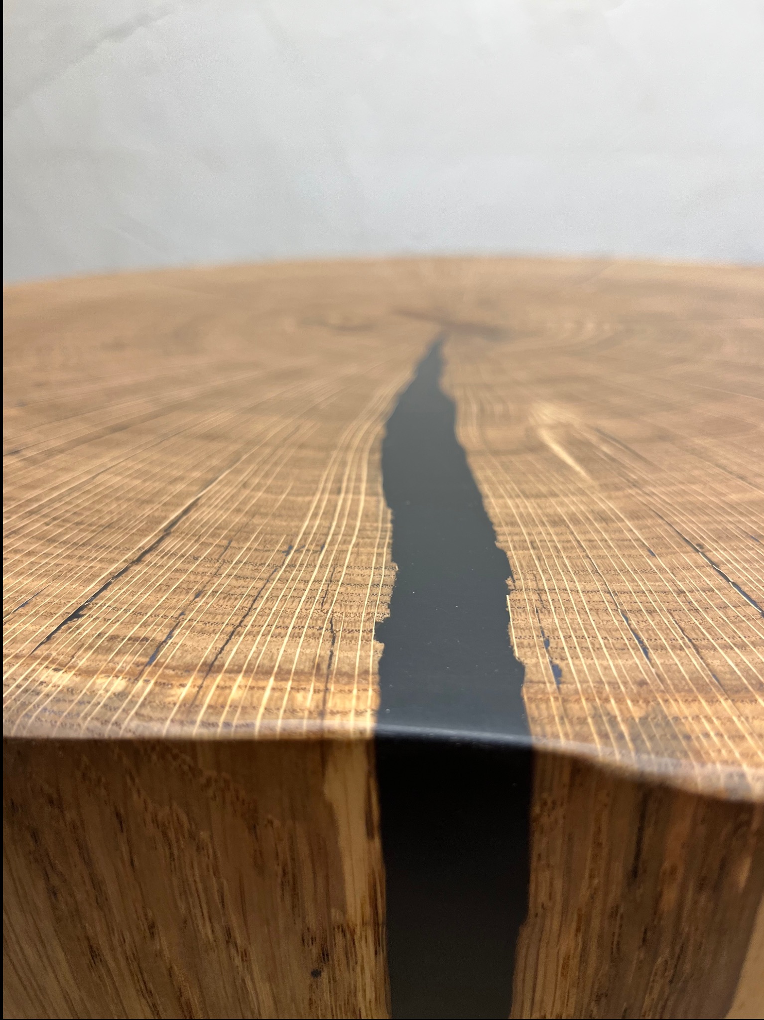 Zbliżenie na drewniany blat z żywicą epoksydową w kolorze czarnym, wypełniającą naturalne pęknięcie w drewnie, ukazujące strukturę drewna i kontrast z gładką powierzchnią żywicy.