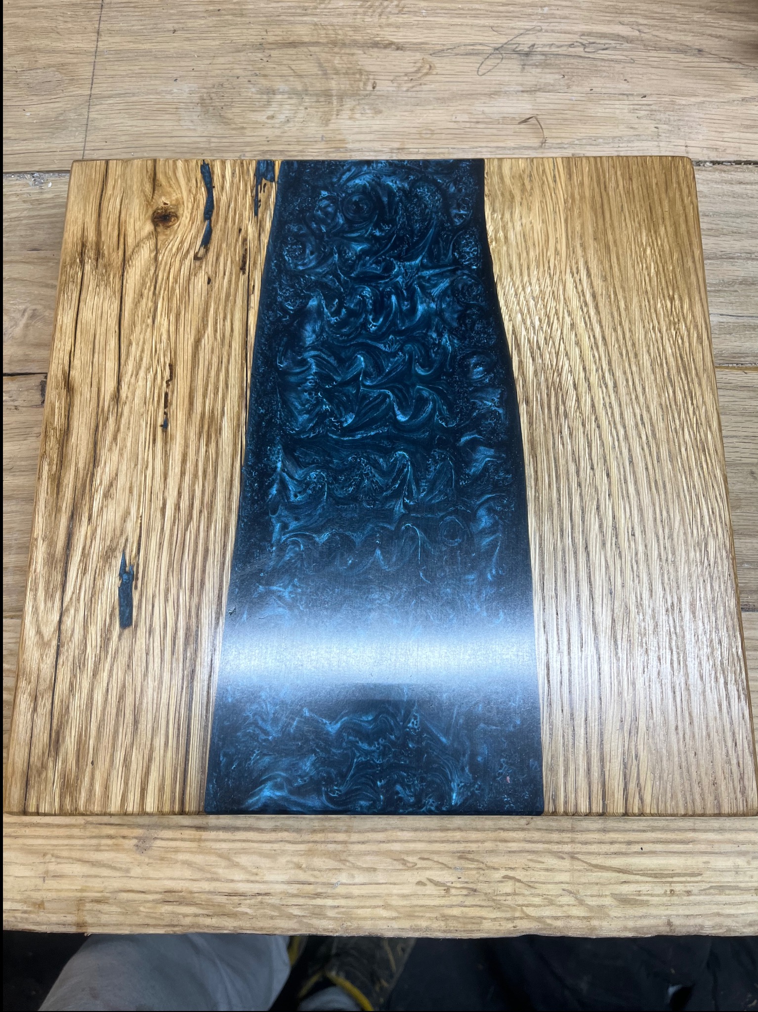 Drewniany blat z wstawką z niebieskiej żywicy epoksydowej o nieregularnym kształcie, ukazujący fakturę drewna i efektowne wzory w żywicy.