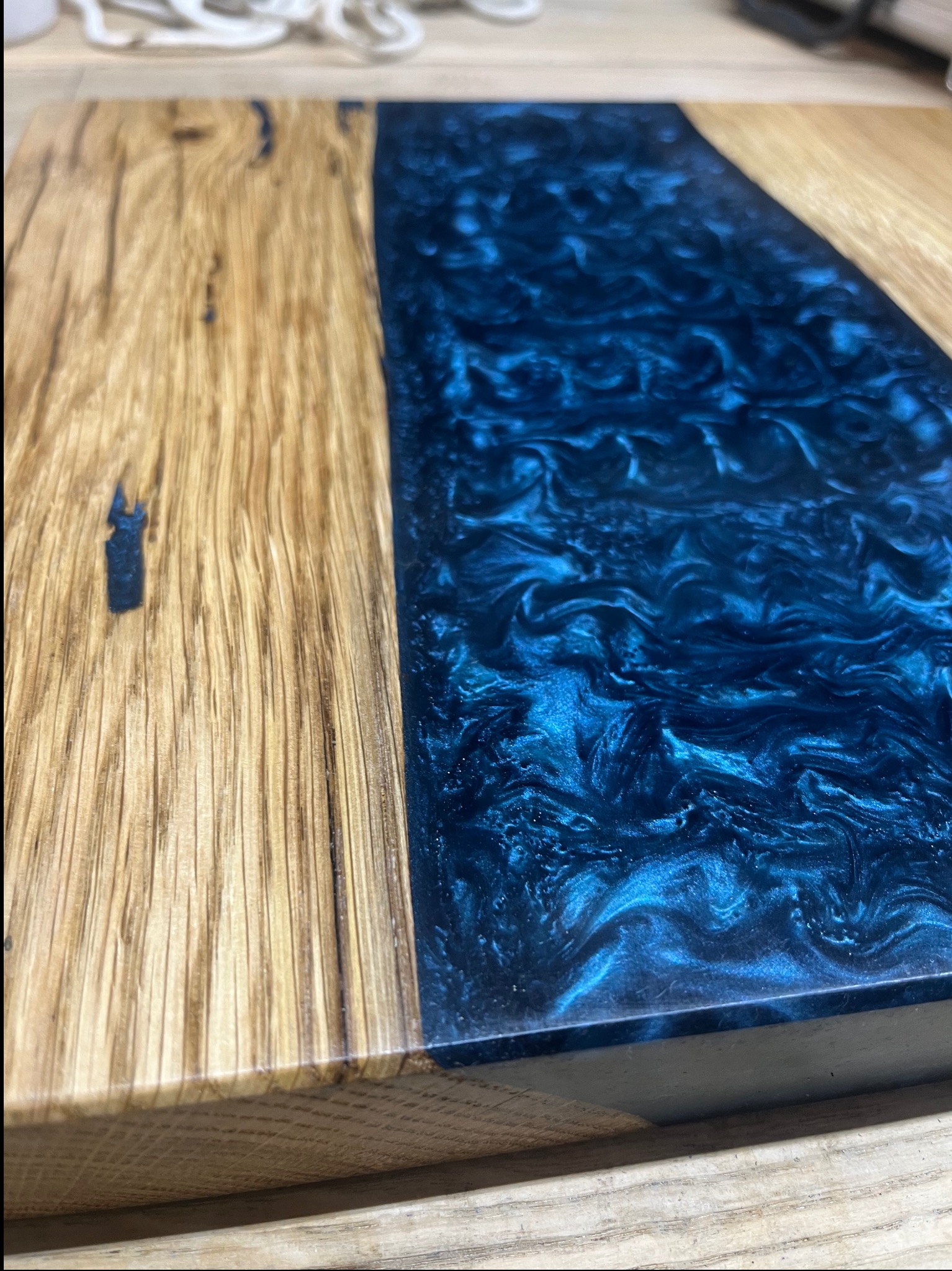 Fragment blatu z drewna dębowego połączonego z żywicą epoksydową w odcieniach błękitu, widoczne unikalne słoje drewna i wzory żywicy.