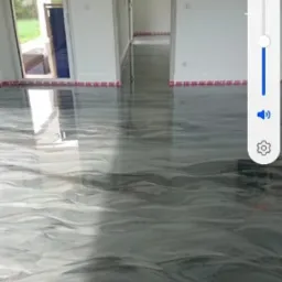 Błyszcząca, szara podłoga żywiczna z marmurkowym wzorem w pustym, jasnym pomieszczeniu z białymi ścianami i widocznymi drzwiami w tle.