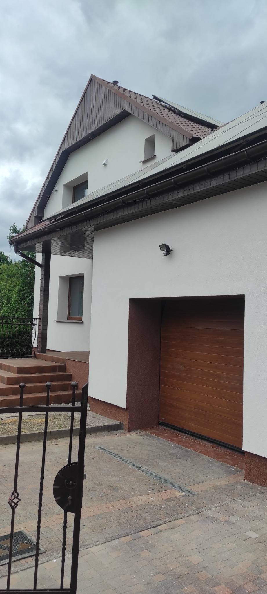 Wykończona elewacja domu jednorodzinnego w Pleszewie, z brązowymi elementami dekoracyjnymi, widoczna brama garażowa i fragment ogrodzenia.