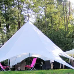 Rozłożony biały namiot imprezowy typu Star Shade z różowymi krzesłami i ciemnymi meblami ogrodowymi na tle zieleni drzew.