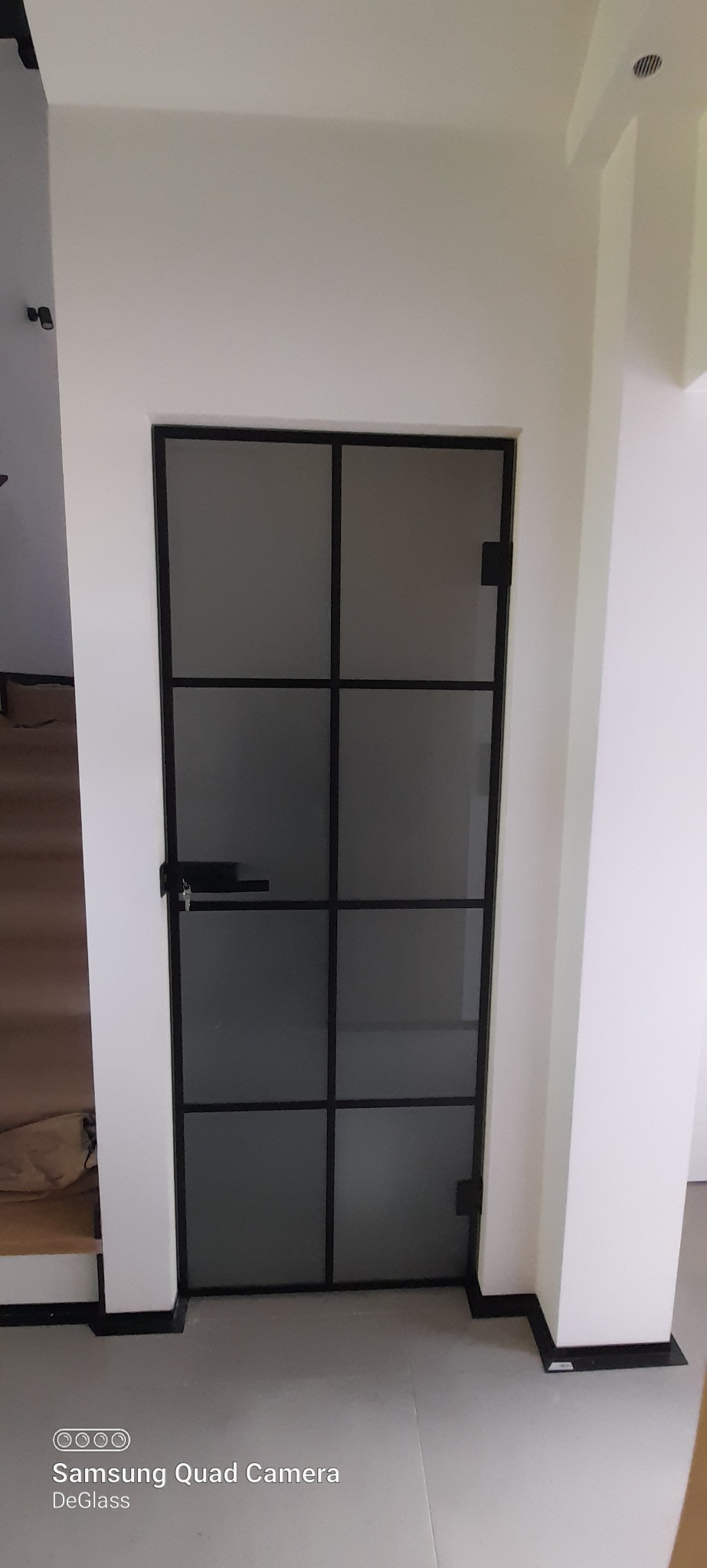 Nowoczesne drzwi wewnętrzne z czarnymi szprosami i matowym szkłem, zamontowane w białej ścianie.