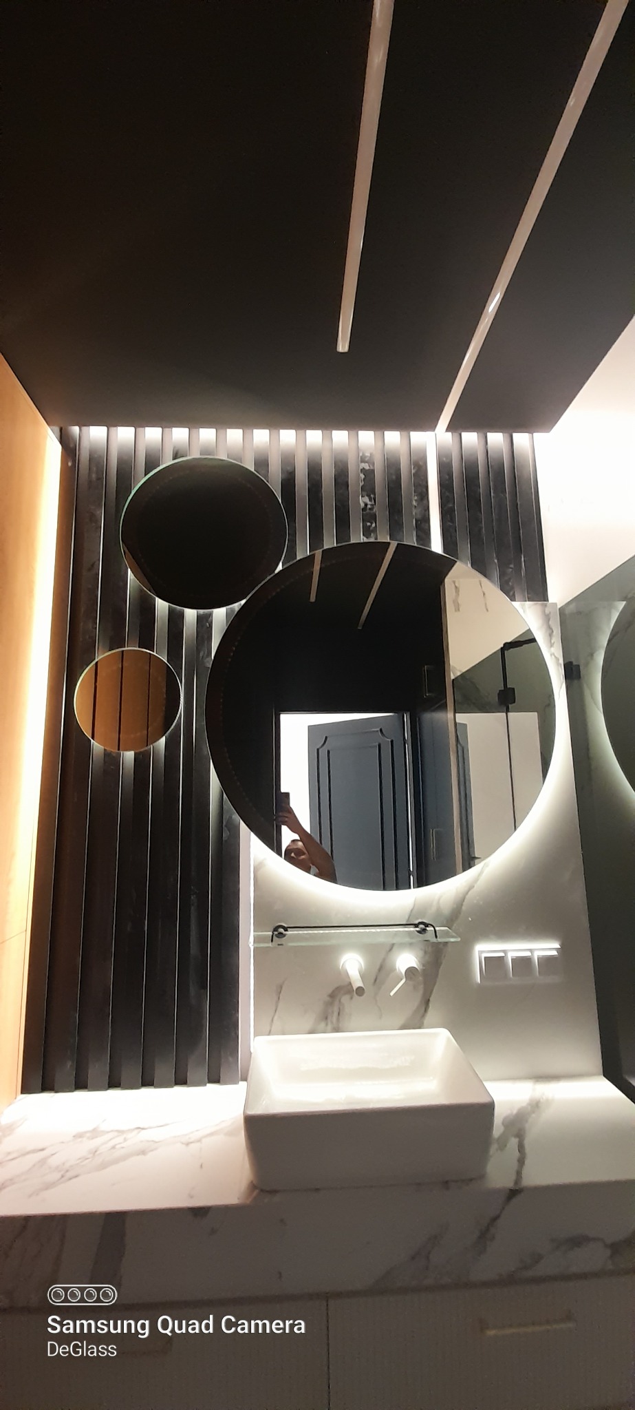 Nowoczesna łazienka z okrągłymi lustrami podświetlanymi LED, marmurowym blatem i kwadratową umywalką nablatową, widoczne pionowe lamele na ścianie.