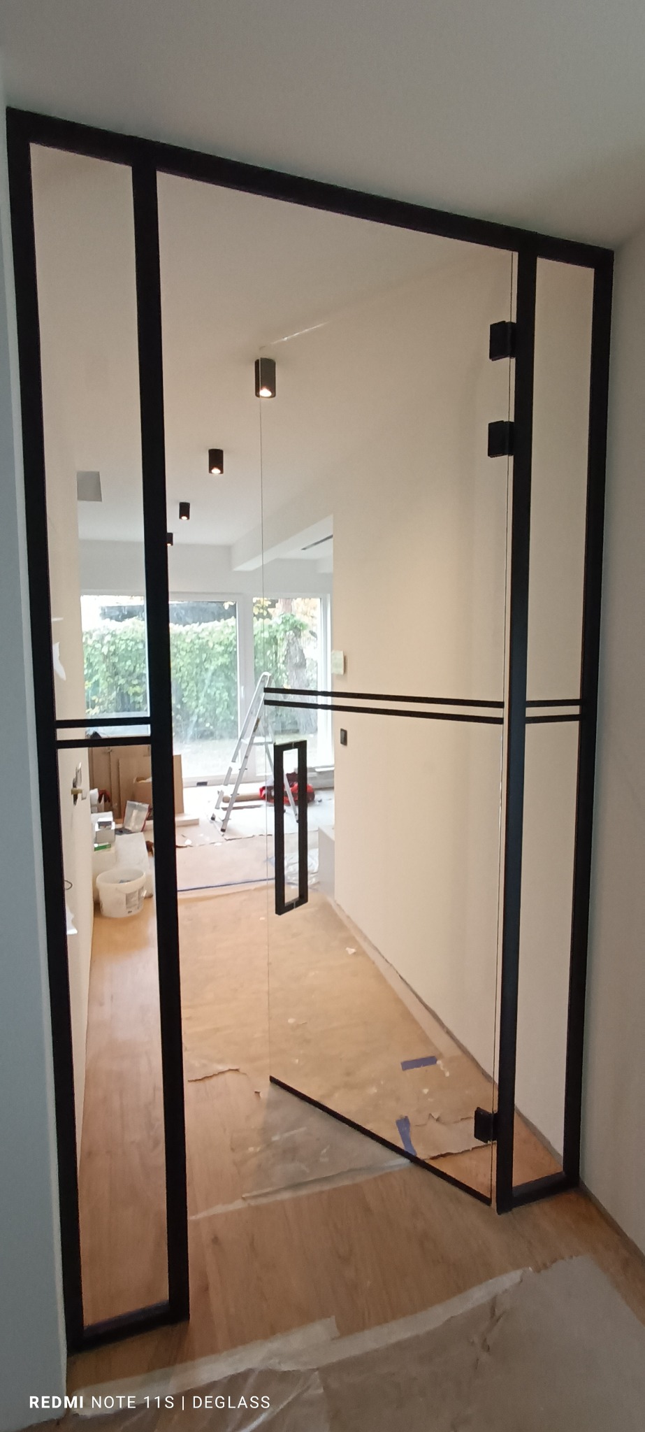 Nowoczesne drzwi wewnętrzne ze szkła z czarną ramą, widoczne ślady prac wykończeniowych na podłodze.