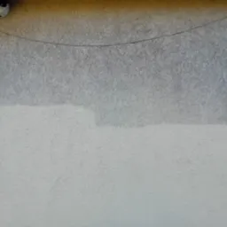 Fragment elewacji budynku po częściowym umyciu, widoczna różnica w kolorze i czystości, kamera monitoringu w lewym górnym rogu.