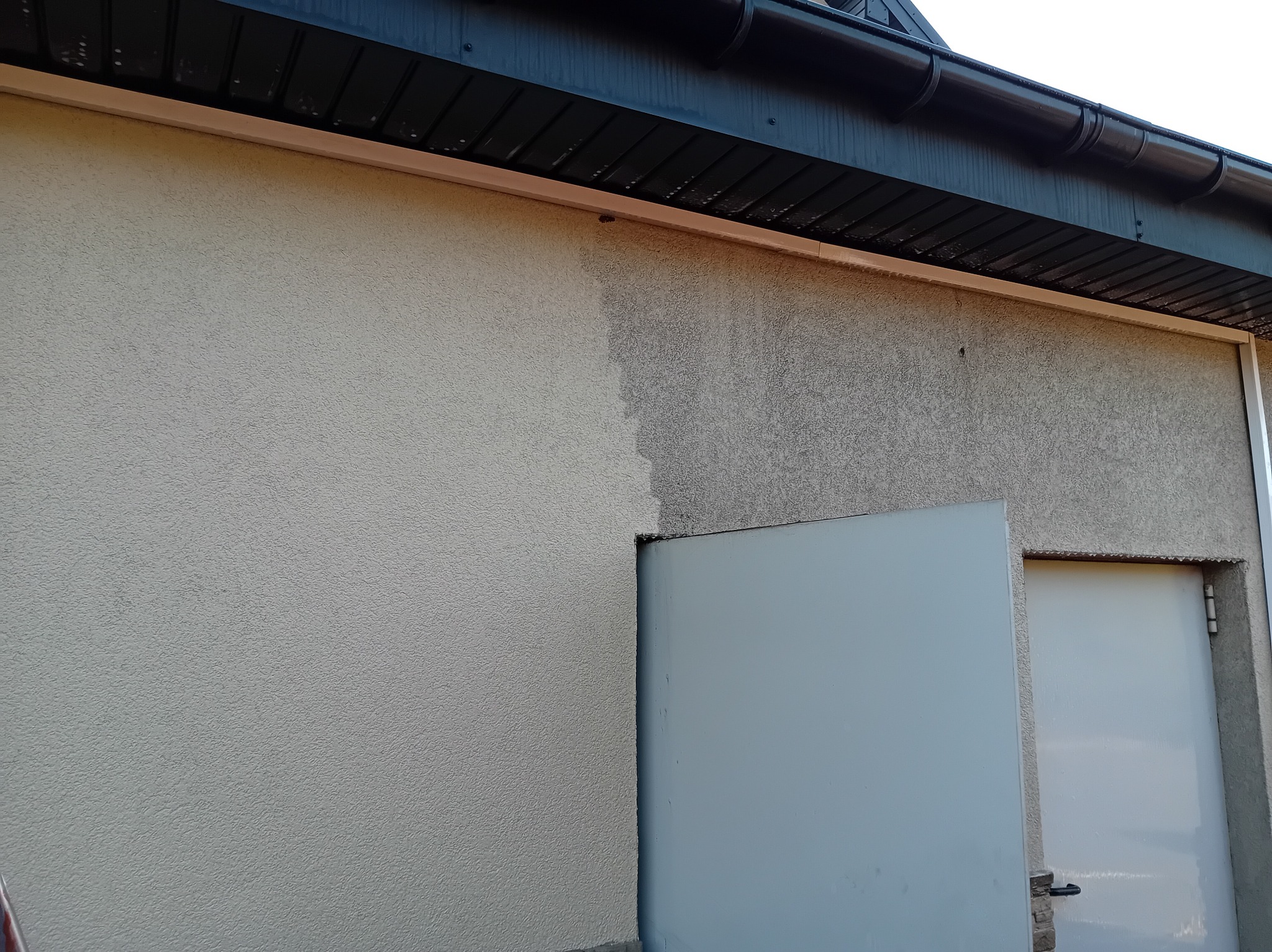 Fragment elewacji budynku przed i po umyciu, widoczna różnica w kolorze i czystości tynku, brama garażowa częściowo otwarta.