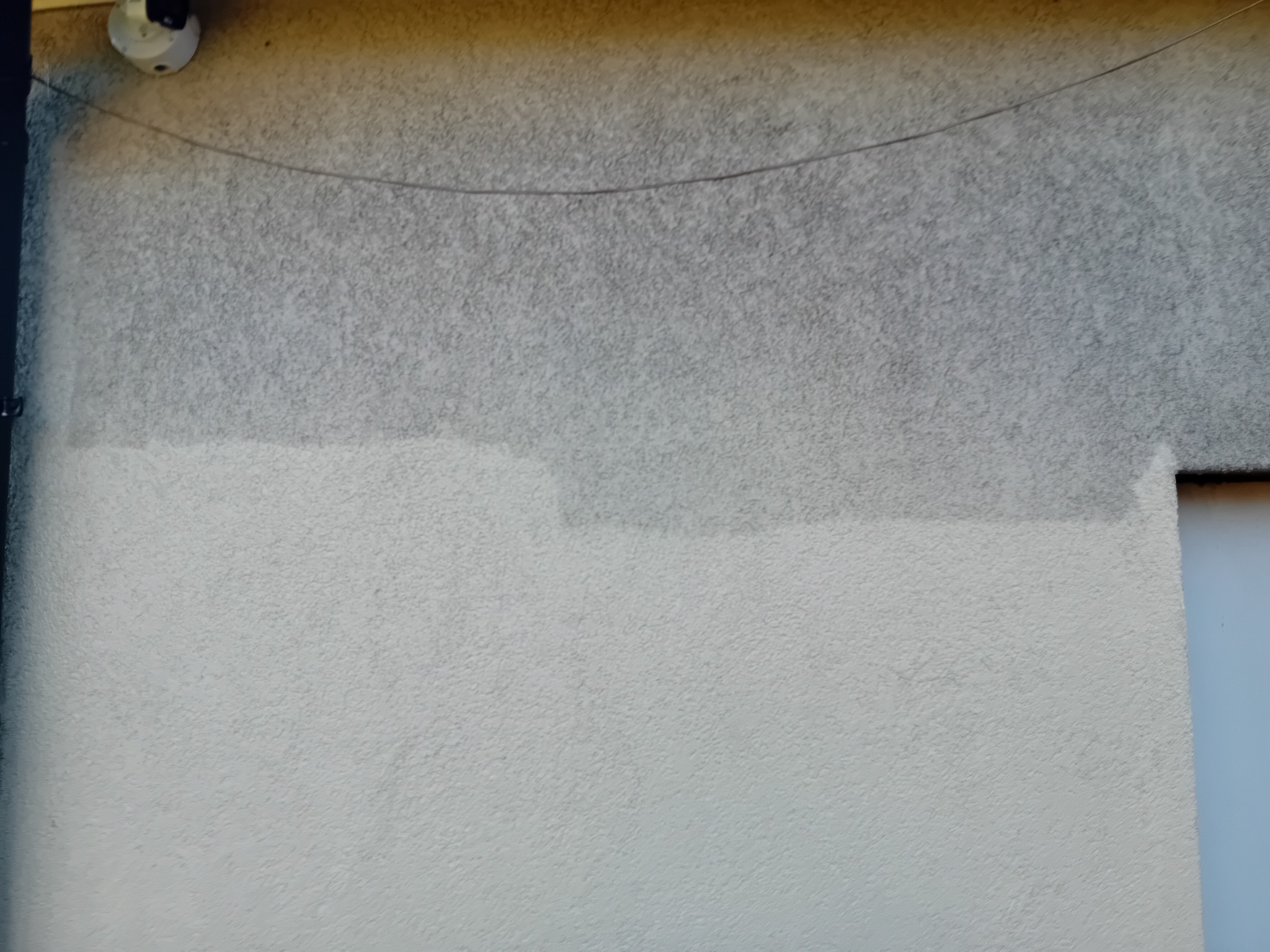 Fragment elewacji budynku po częściowym umyciu, widoczna różnica w kolorze i czystości, kamera monitoringu w lewym górnym rogu.