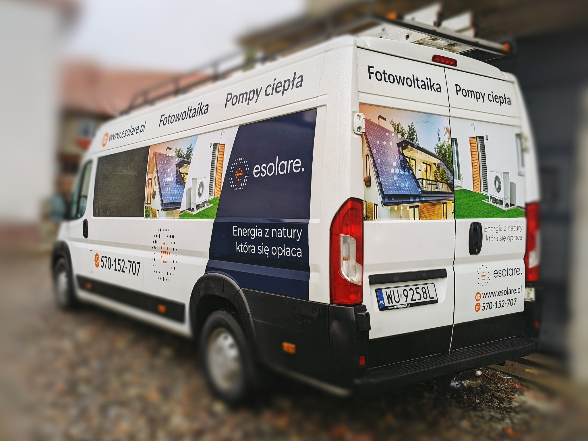 Biały samochód dostawczy oklejony grafiką reklamową firmy Esolare, prezentującą fotowoltaikę i pompy ciepła, z widocznym numerem telefonu i adresem strony internetowej.