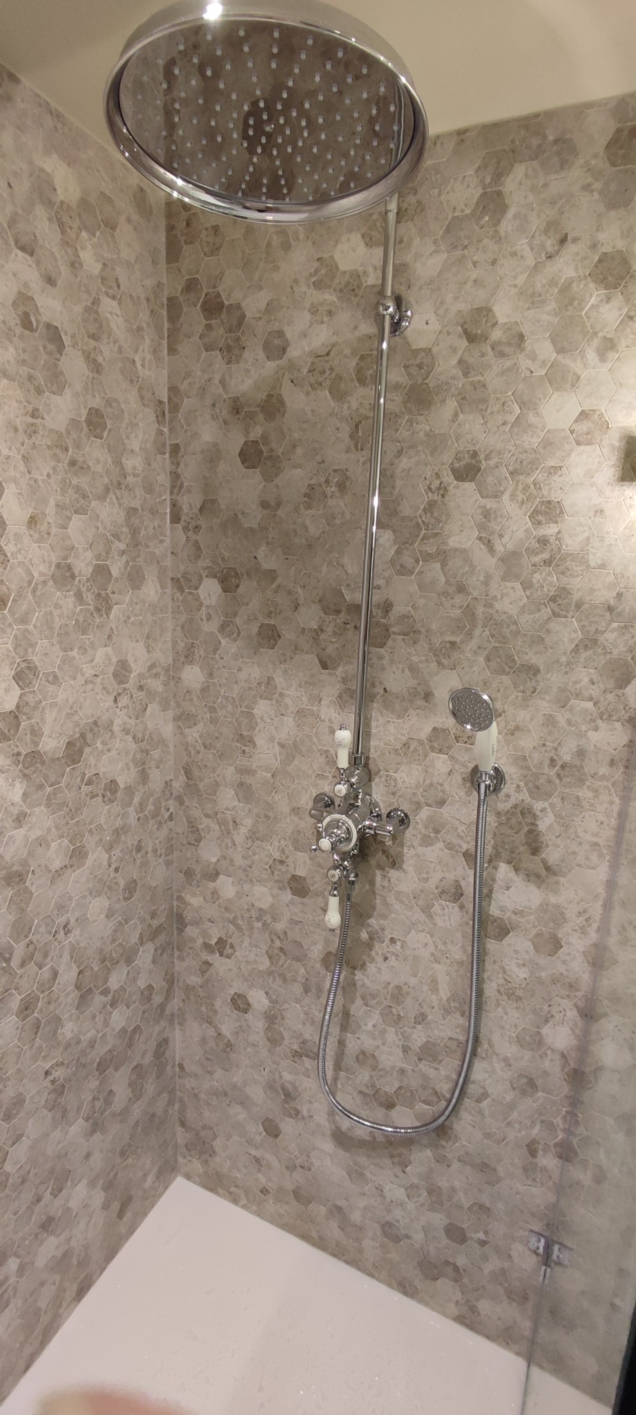 Nowoczesna kabina prysznicowa z deszczownicą i zestawem armatury w stylu retro, wykończona heksagonalnymi płytkami w odcieniach beżu i szarości.