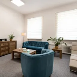 Jasne, minimalistyczne wnętrze gabinetu terapeutycznego z turkusowymi meblami wypoczynkowymi, drewnianą komodą i stonowaną dekoracją.