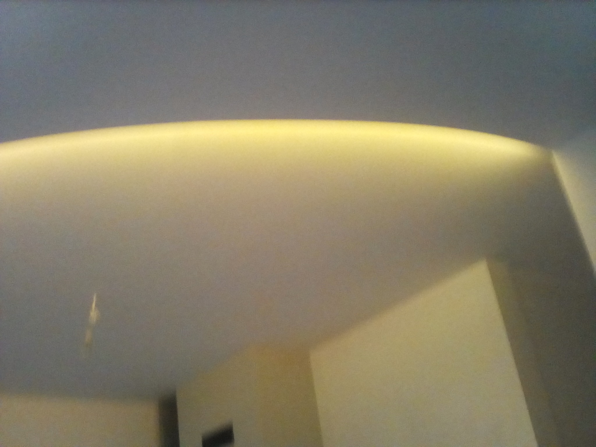 Fragment sufitu z wbudowanym oświetleniem LED tworzącym łuk, widok pod kątem, ściany w tle w odcieniach beżu.