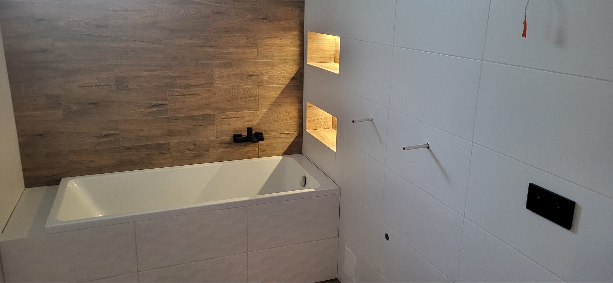 Nowoczesna łazienka po remoncie: białe i drewnopodobne płytki, podświetlane wnęki, czarna armatura. Minimalistyczny design z dbałością o detale.