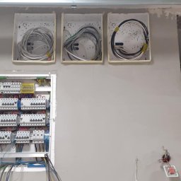 EL-KOP Paweł Koper - Rozdzielnica elektryczna z bezpiecznikami i okablowaniem w trzech puszkach na ścianie podczas prac wykończeniowych, widoczne przewody i elementy instalacji.
